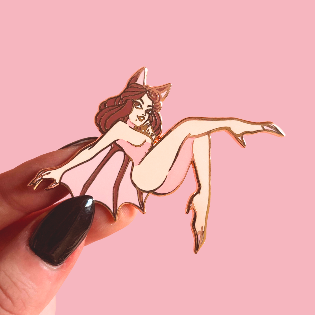 Enamel pin of a stylized female figure with bat wings on a pink background