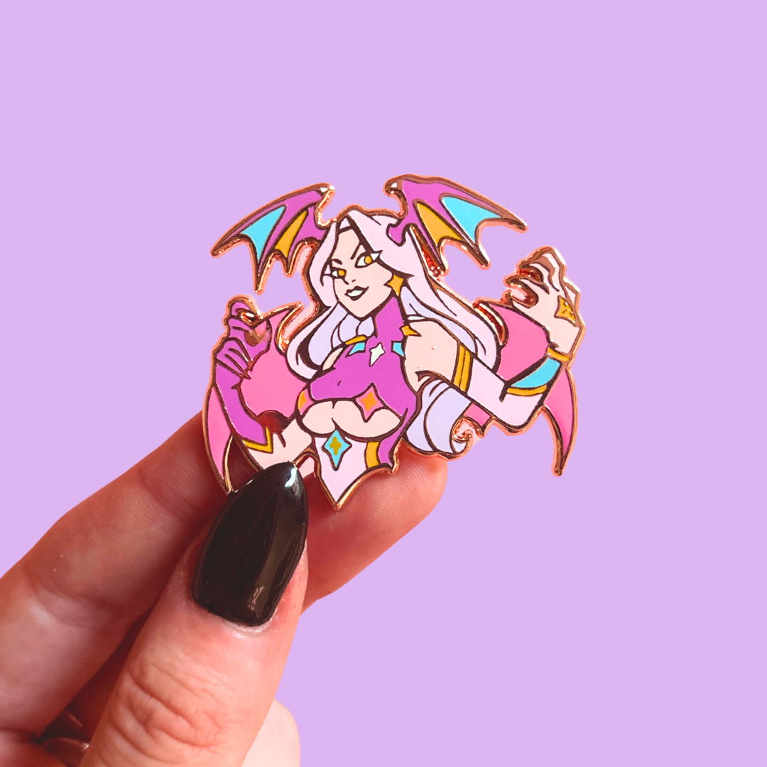 Colorful character pin with wings on head and back held by a hand against a purple background