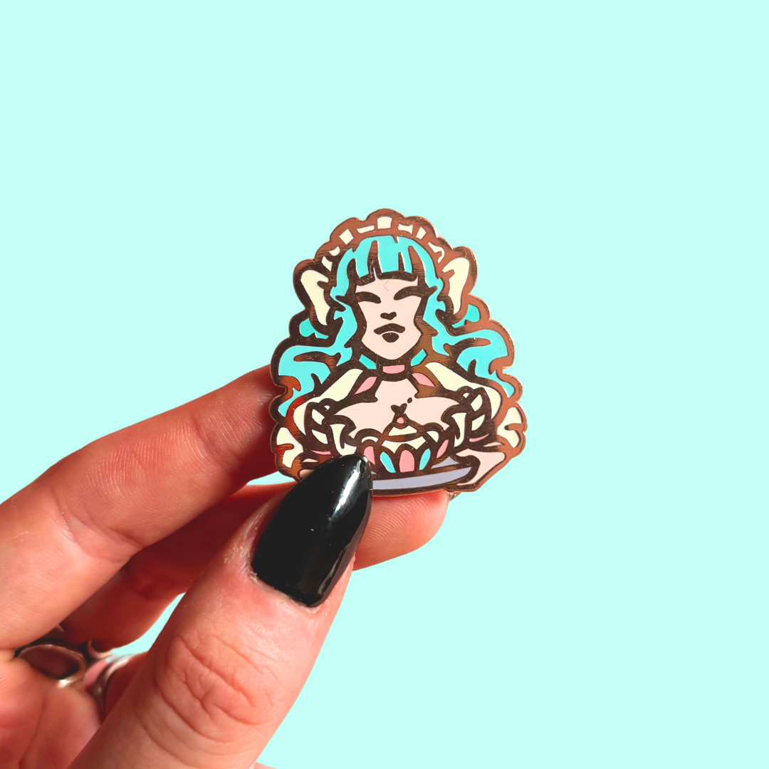 Hand holding a colorful maid enamel pin against a light blue background