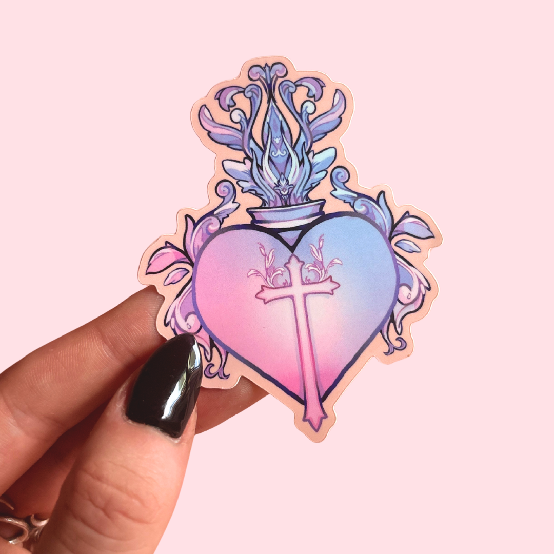 Sticker with a heart design featuring a cross and floral elements held by a hand on a pink background