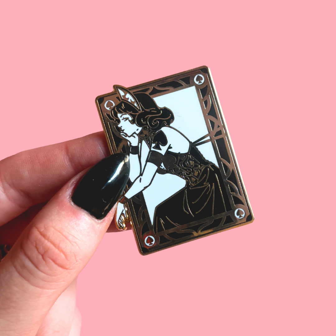 Enamel pin of a Girl in playing card design held by a hand against a pink background
