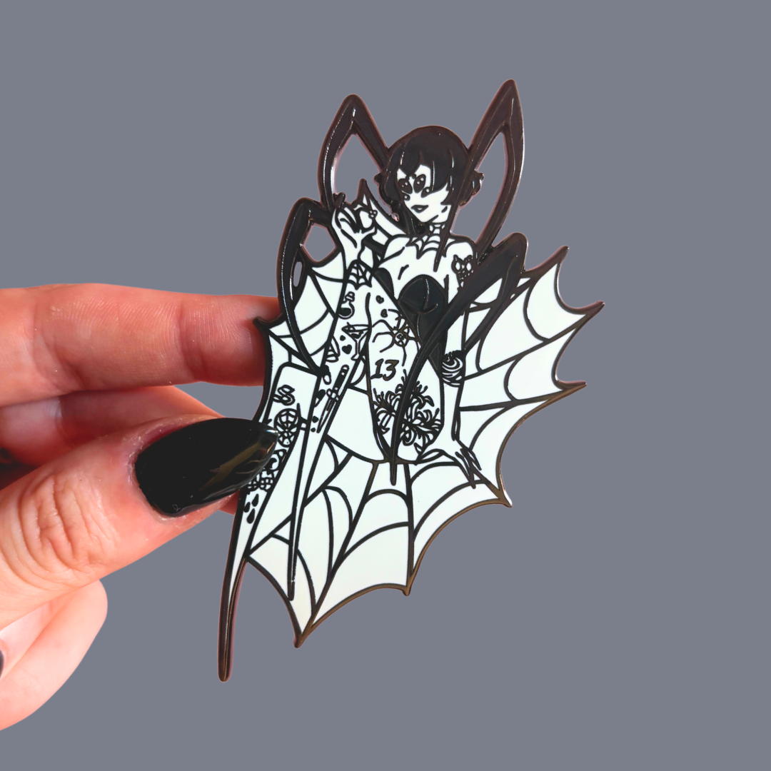 Hand holding a black and white spider-shaped woman pin against a gray background