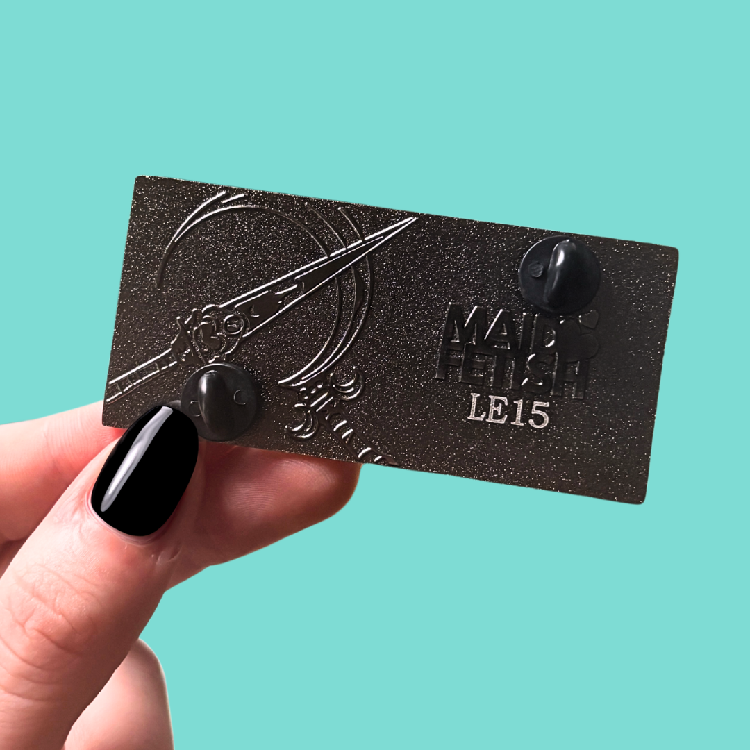 Black back of enamel pin engraved with a weapon held by a hand against a teal background