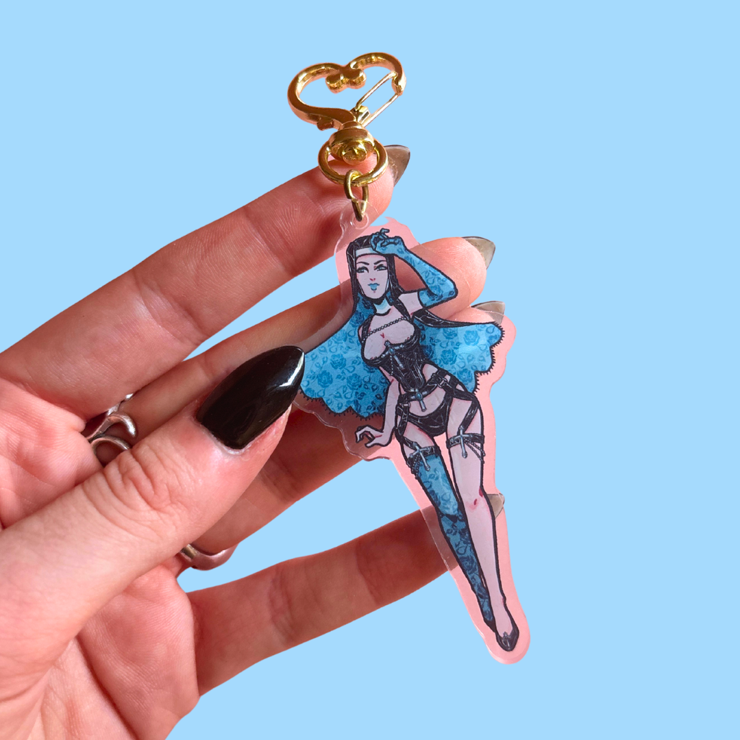 Hand holding a keychain with a blue fairy design against a light blue background