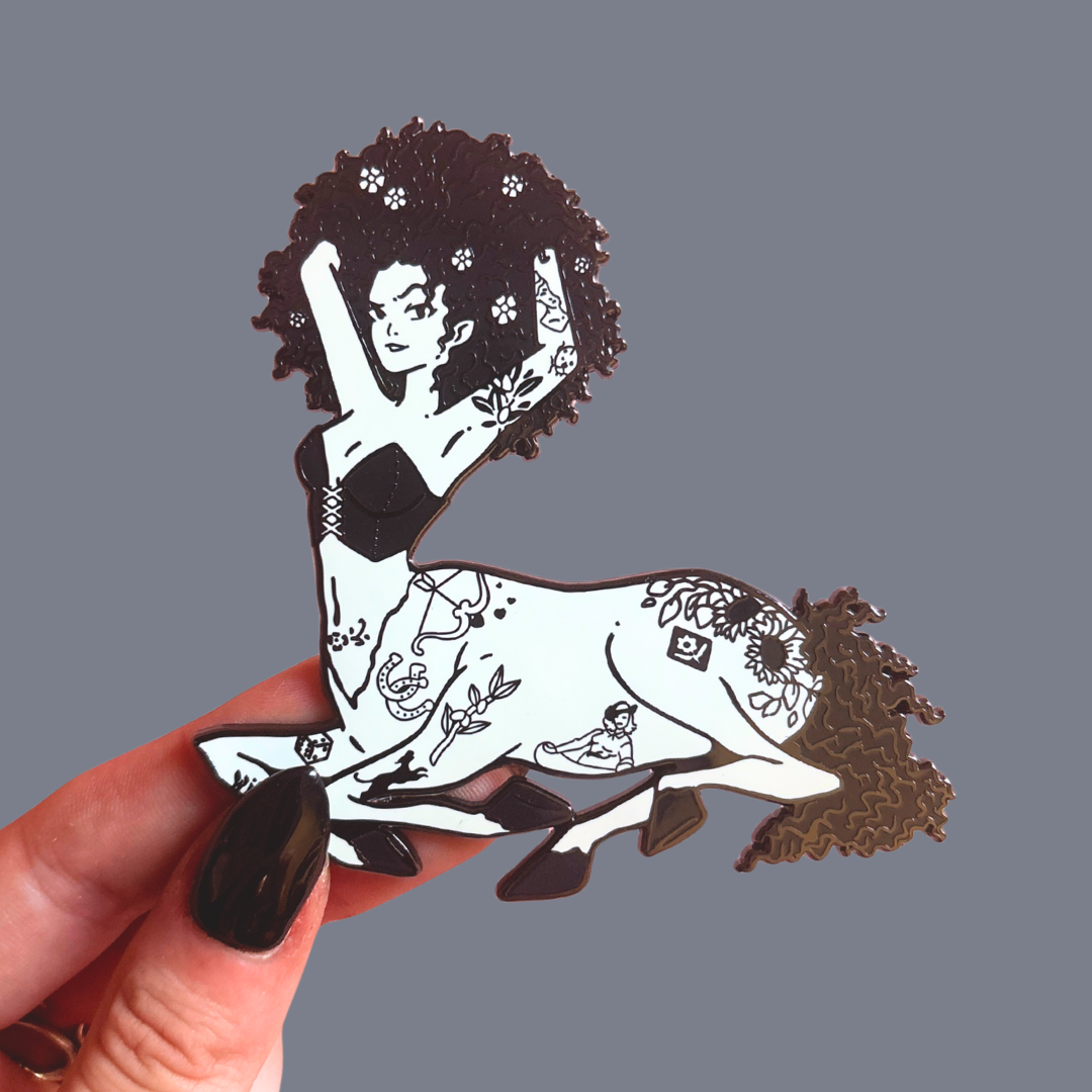 Pin of female Centaur, held by a hand against a gray background