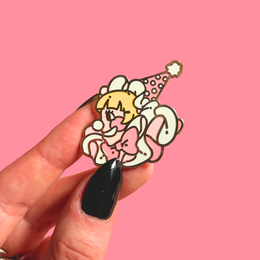 Hand holding a clown cartoon character pin with a party hat against a pink background