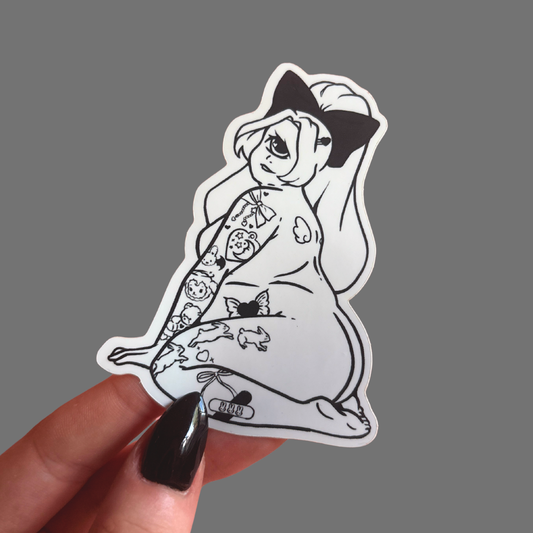 Sticker of a cyclops girl with tattoos held by a hand on a gray background
