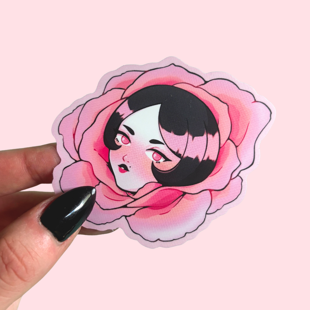 Sticker of a character with black hair and black eyes on pink flower held by a hand on a pink background
