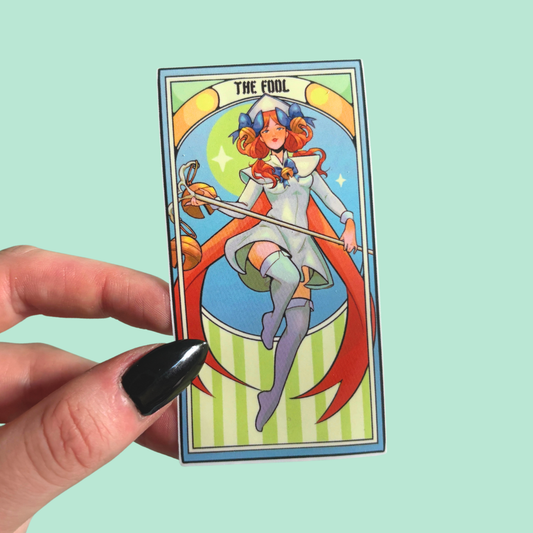 Sticker featuring 'The Fool' from a tarot deck held by a hand against a light blue background