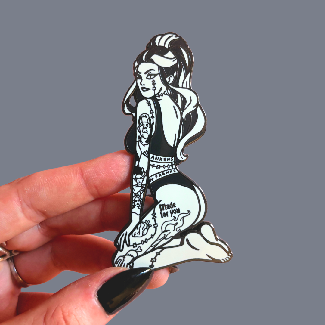 Black and white female Frankenstein pin held by a hand against a gray background
