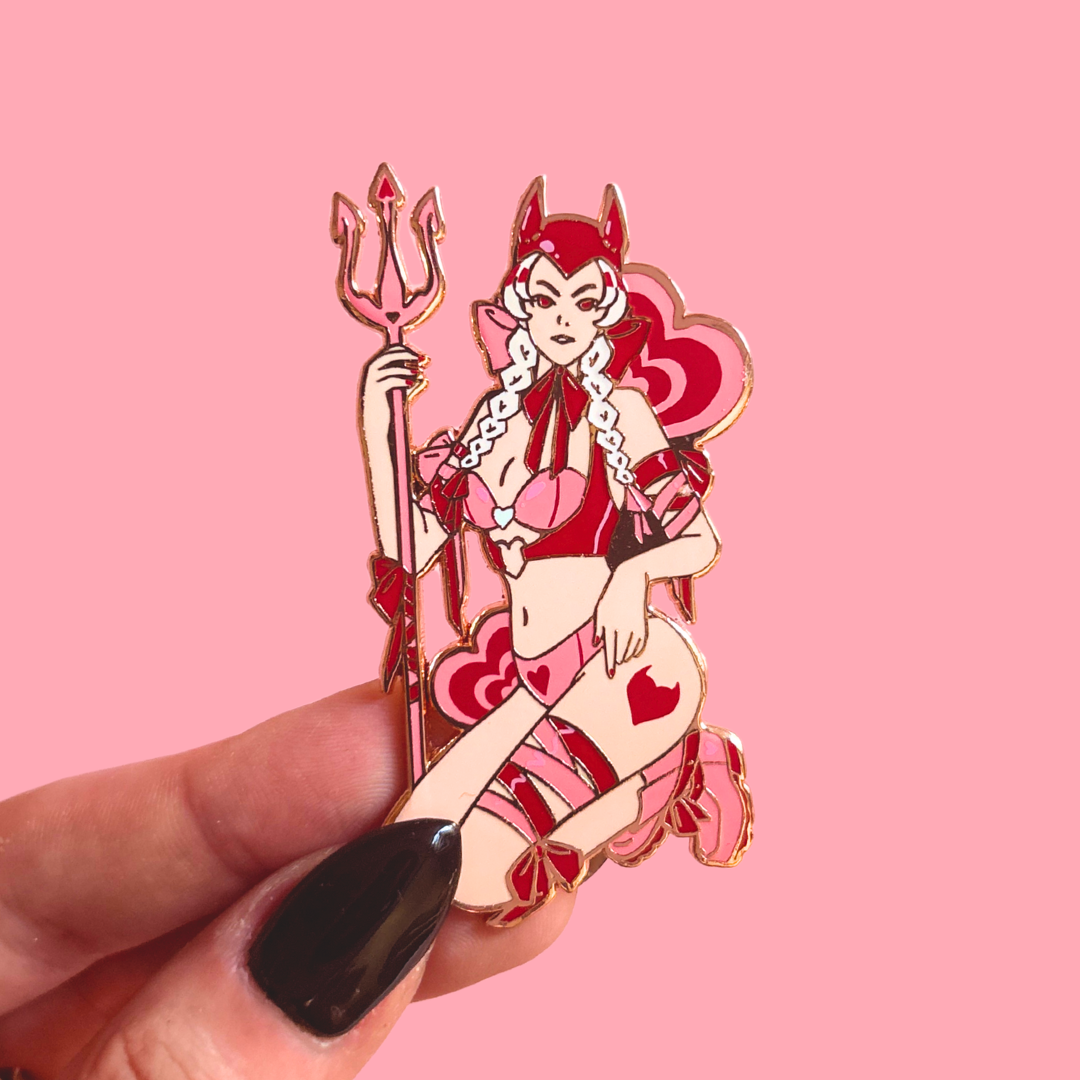 Pin with a stylized female devil character holding a trident on a pink background