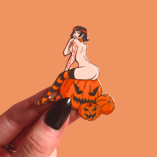 Halloween-themed pin with a woman on pumpkins held by a hand against an orange background