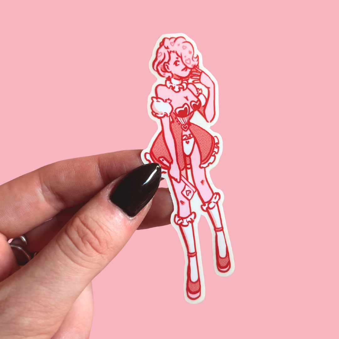 Hand holding a red and white illustrated sticker of a character on a pink background