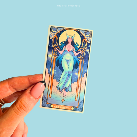 Hand holding a tarot card sticker with a stylized figure against a light blue background