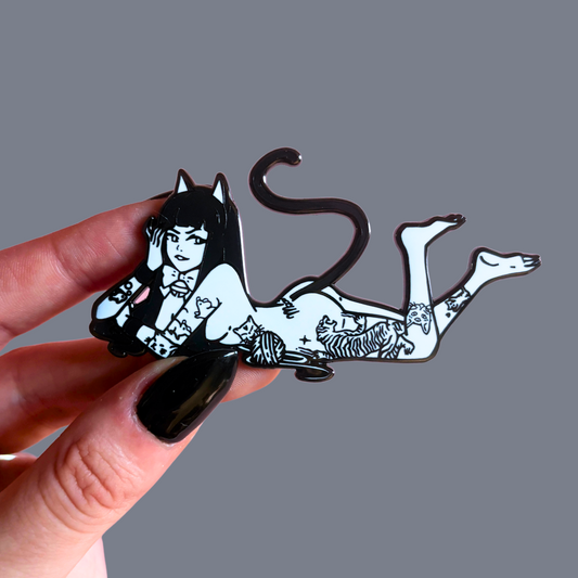 Hand holding a black and white pin of a cat-like creature with a person's face.