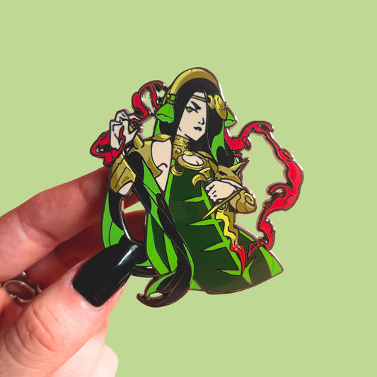 Hand holding a colorful character pin with a green and red design on a light green background