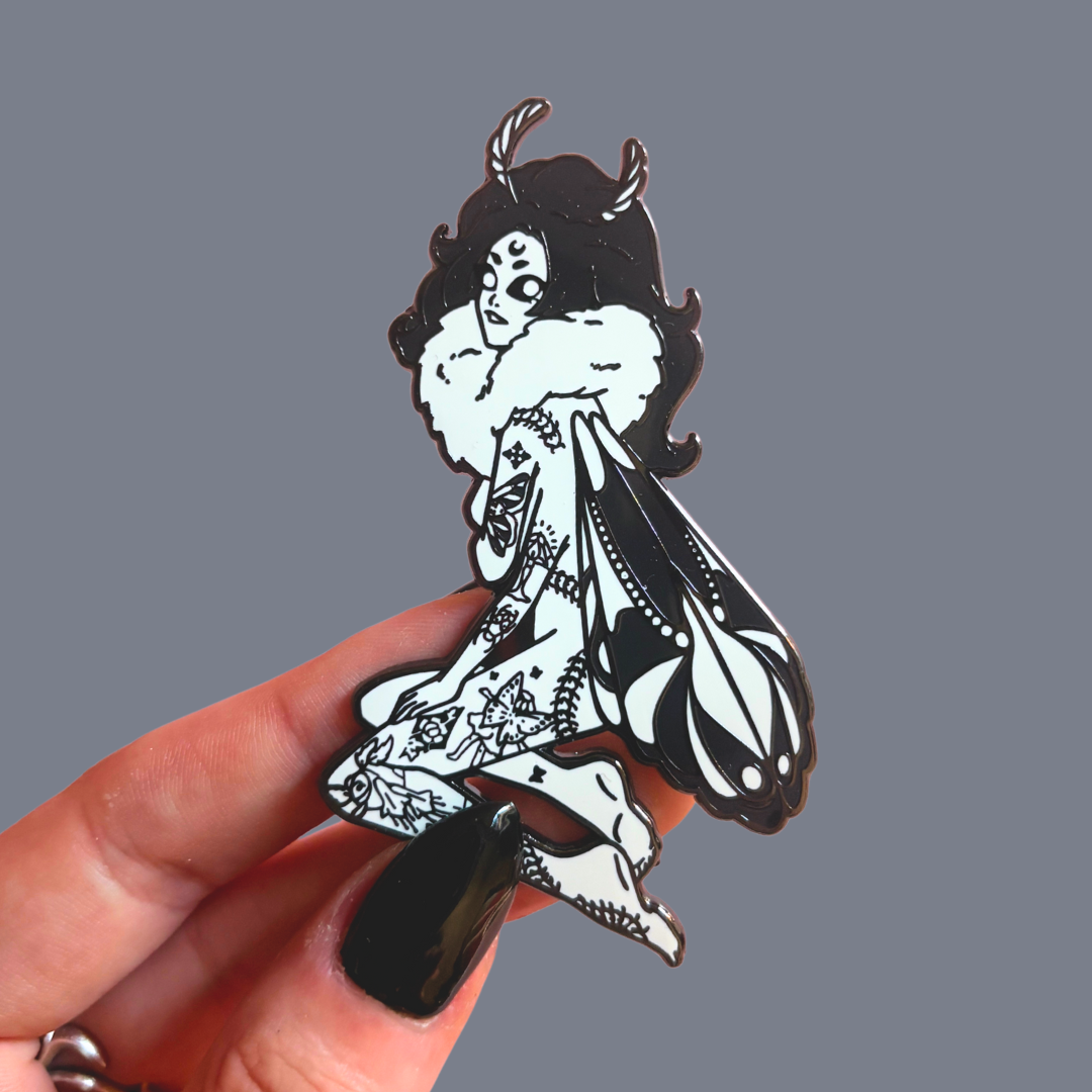 Black and white illustration of a moth girl character held by a hand against a gray background
