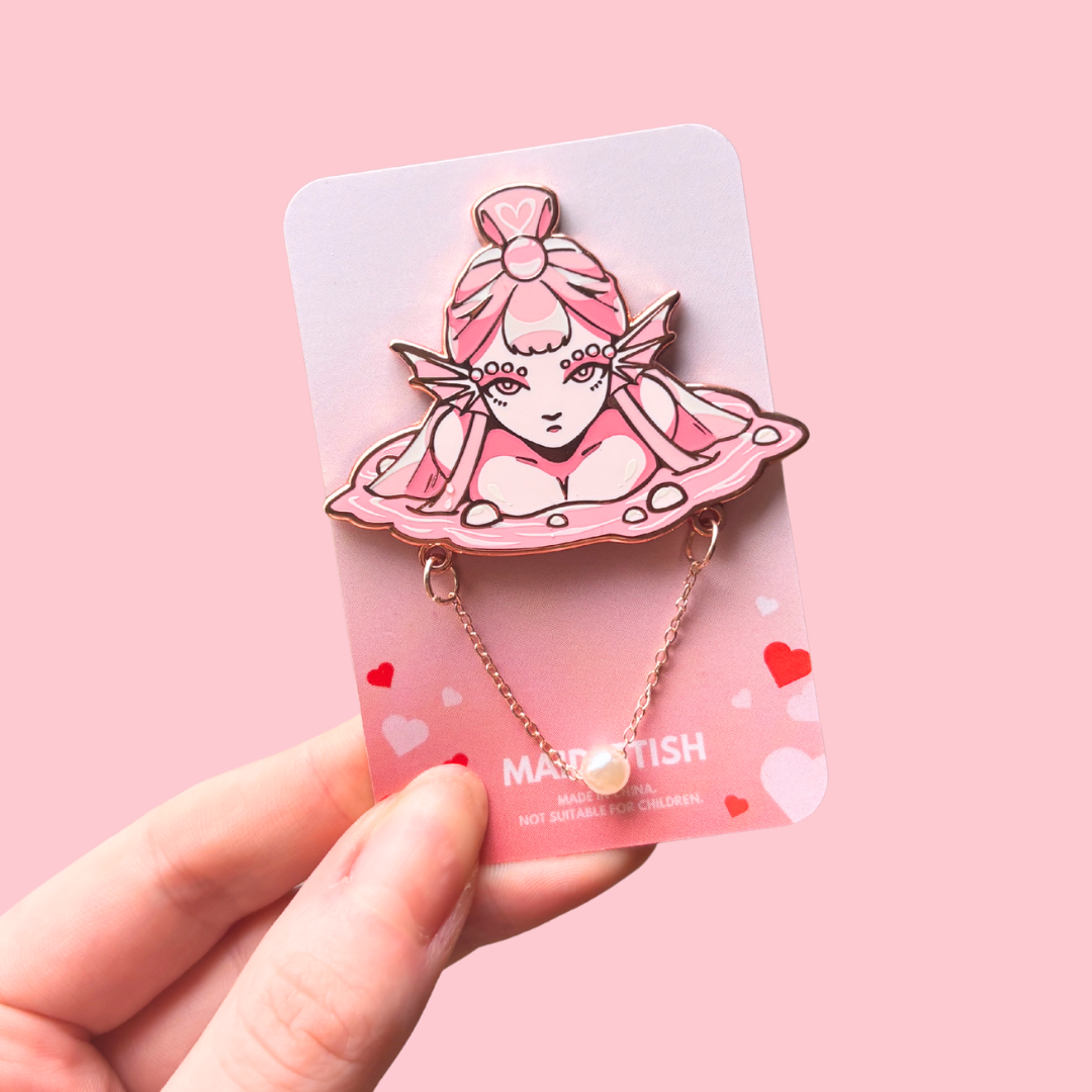Pin with an illustrated character on a pink card held by a hand against a pink background