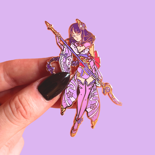 Colorful purple character pin held by a hand against a purple background