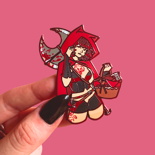 Enamel pin of a character in red hood and black outfit against a pink background