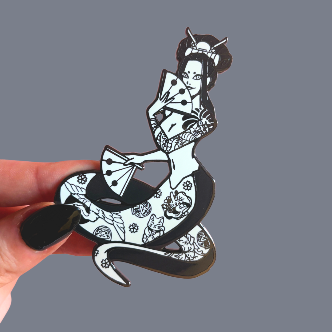 Pin with a design of a snake woman, held against a gray background