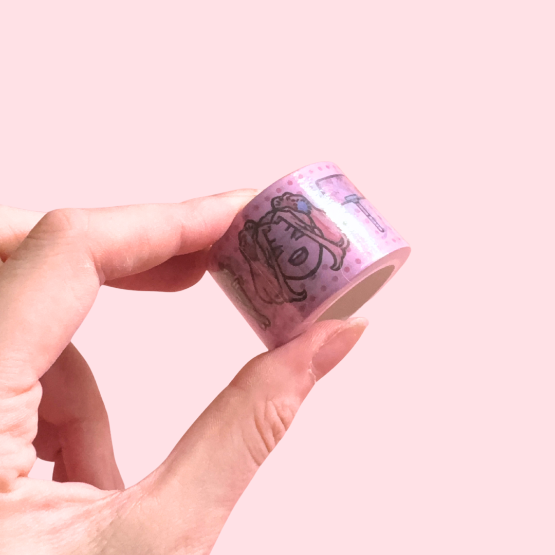 Hand holding a roll of pink decorative tape with cartoon character design on a pink background