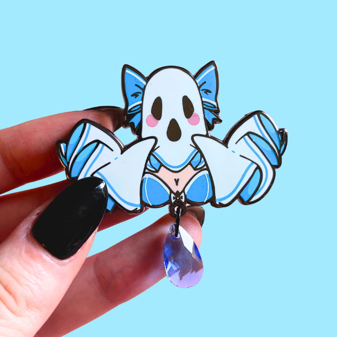 Cartoon ghost pin with blue accents held by a hand against a light blue background