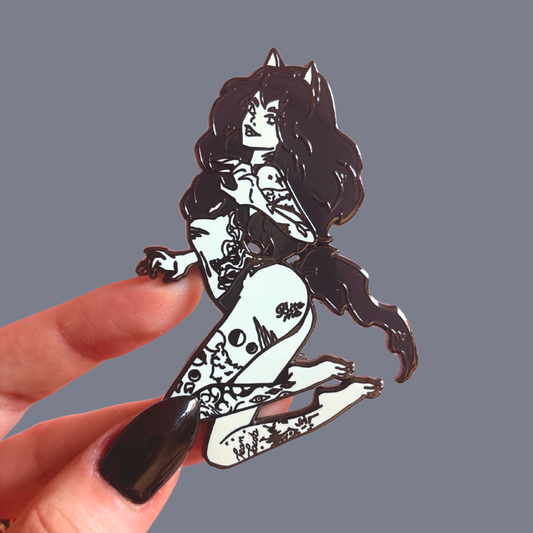 Hand holding a black and white illustration of a stylized wolf girl character pin against a gray background