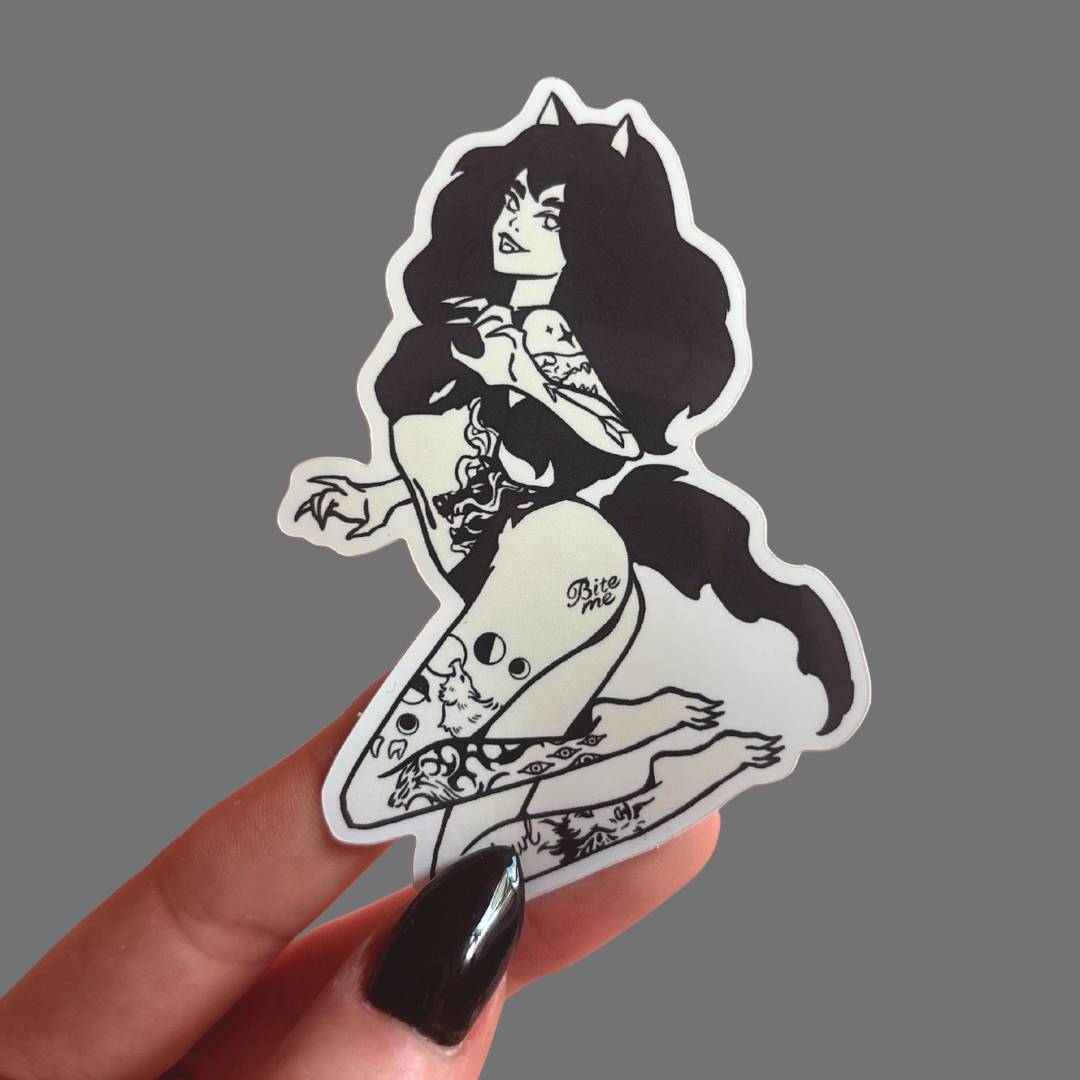Sticker of a stylized wolf woman with tattoos held by a hand against a gray background