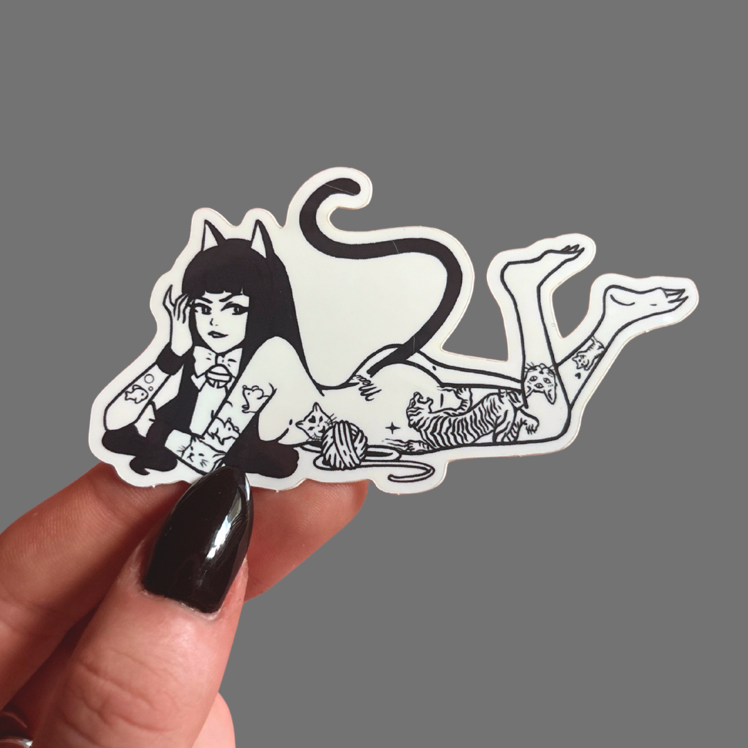 Sticker of a stylized cat-like figure held by a hand against a gray background